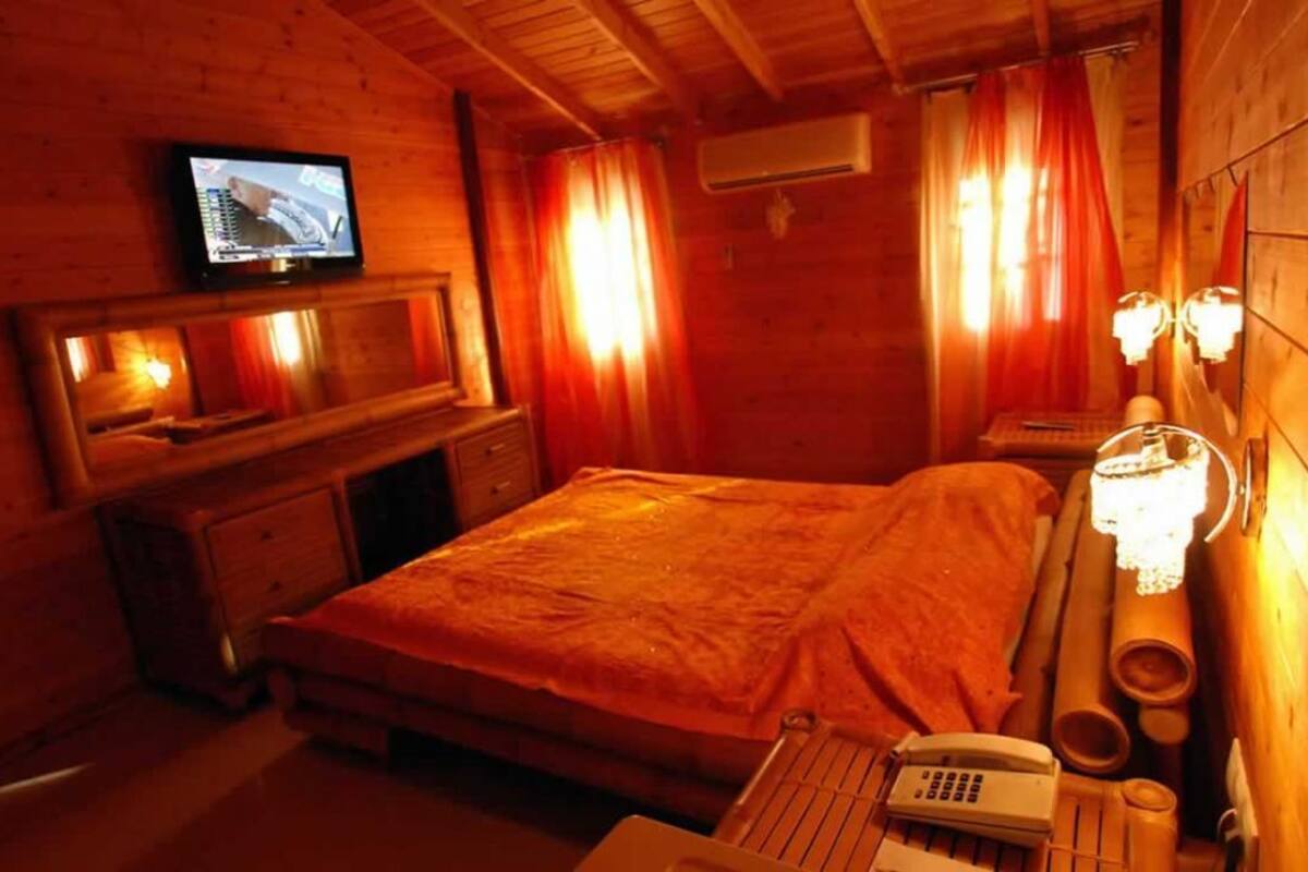 A cozy wooden room with a bed, a television mounted on the wall, and a desk with a telephone.