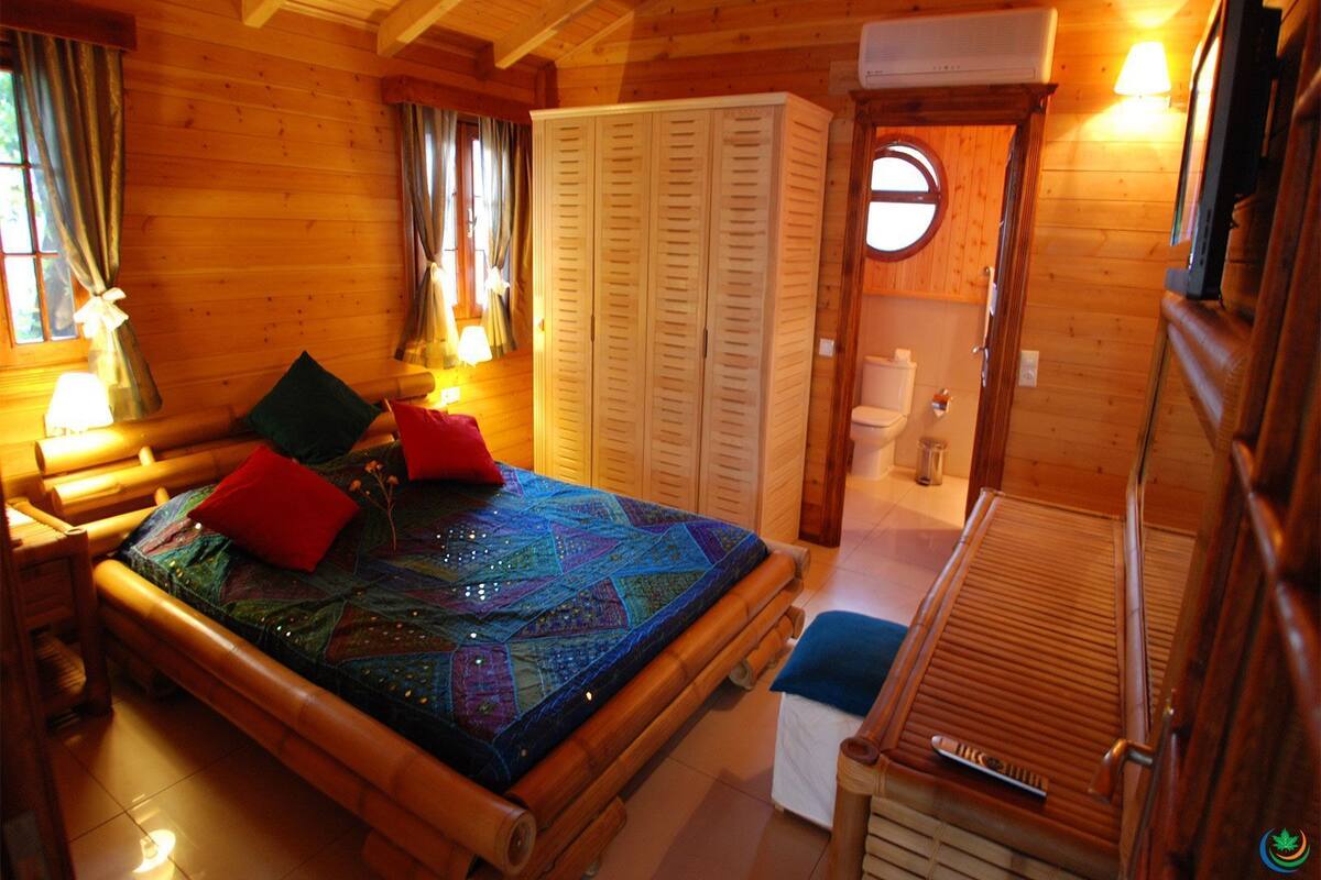 A wooden cabin room with a bed, a small table, and a bathroom.