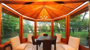 Un belvédère en bois, doté d’une table et de chaises, entouré de murs de verre qui offrent une vue sur un jardin.