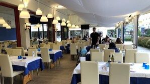 Un restaurant dont les tables sont recouvertes de nappes bleues, avec des chaises blanches et des lampes suspendues.