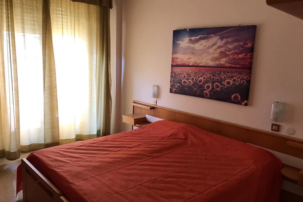Une chambre d’hôtel avec un lit, un bureau et un tableau représentant un coucher de soleil sur un champ de tournesols.