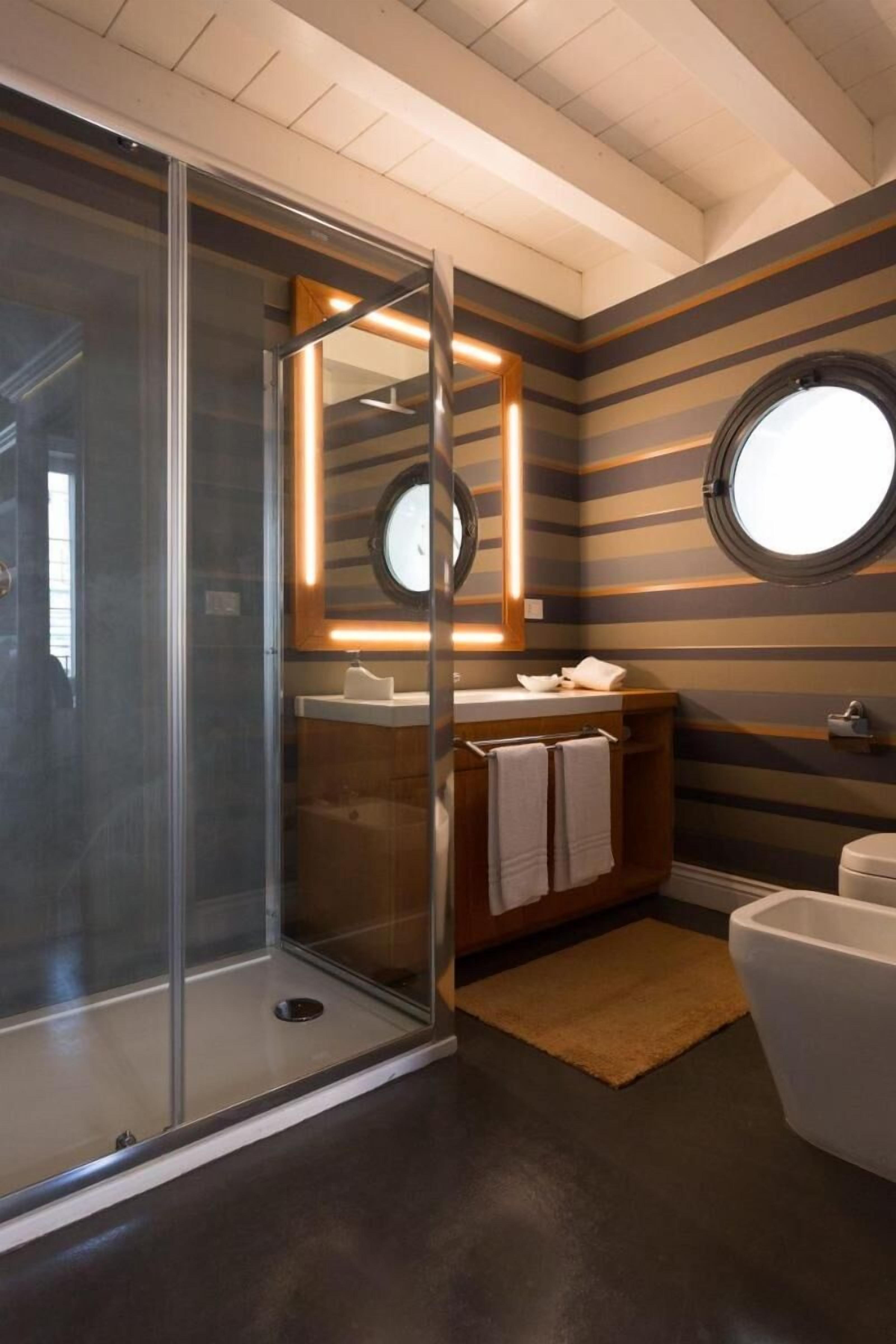 A modern bathroom with a glass-enclosed shower, a round mirror, and striped walls.