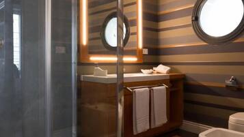 A modern bathroom with a glass-enclosed shower, a round mirror, and striped walls.