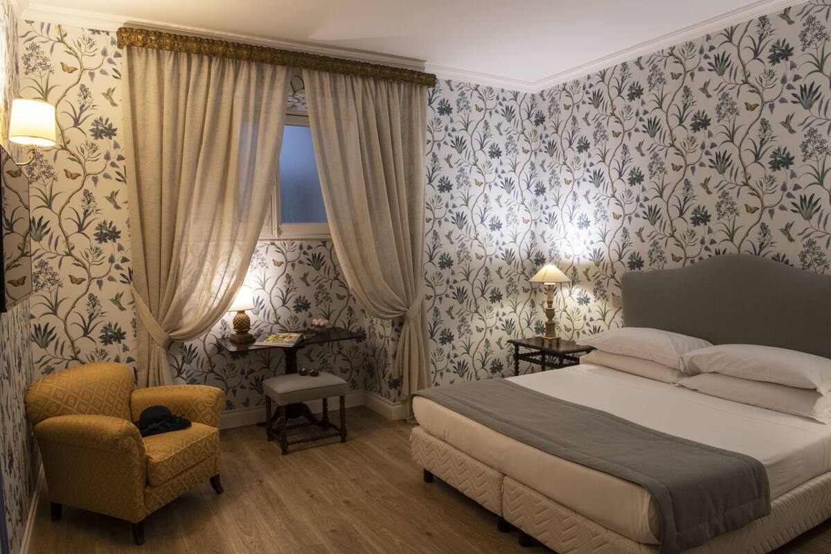 Quarto com cama, cadeira, escrivaninha e janela com cortinas.