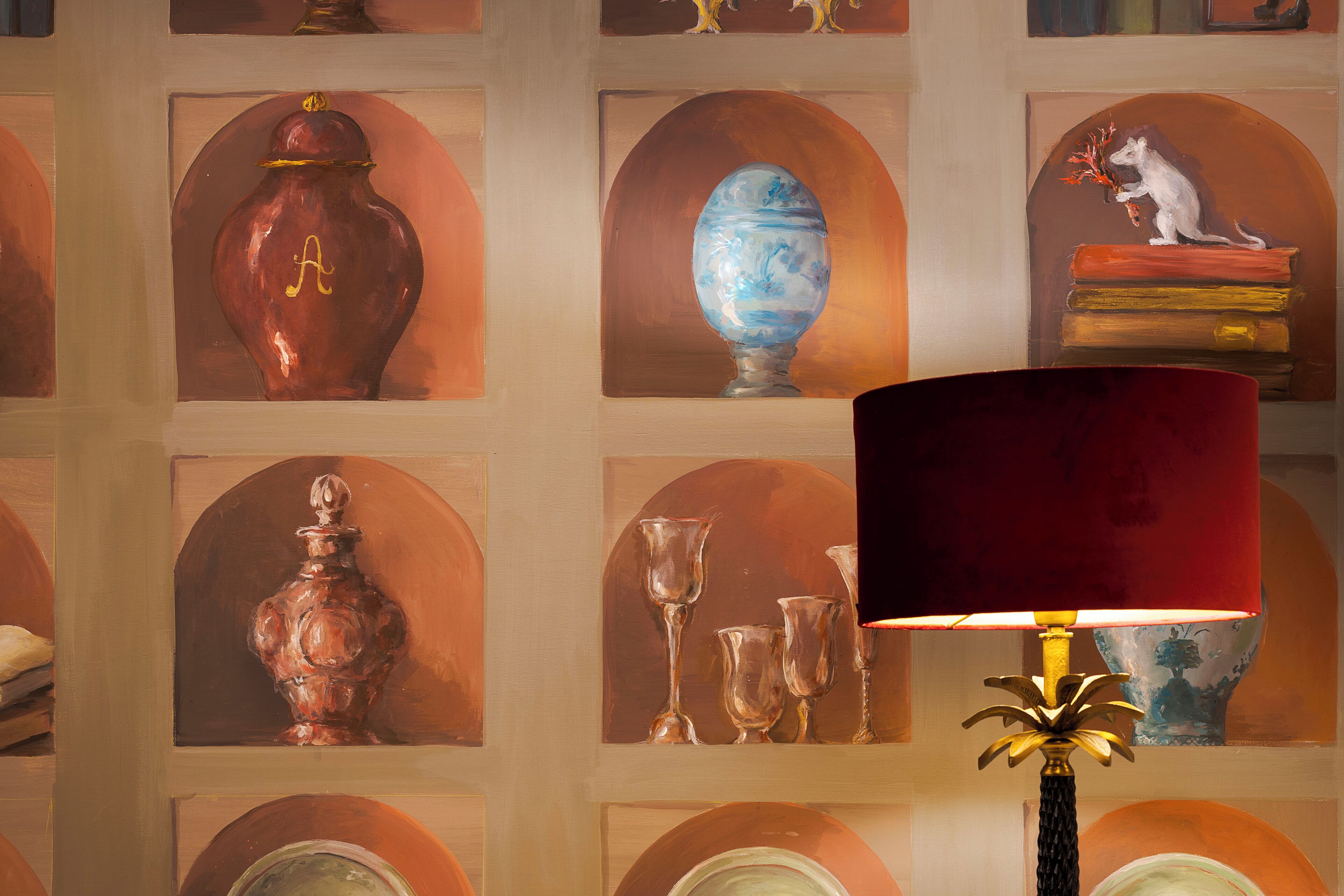A wall with multiple framed artworks, including vases and a sculpture, and a red lamp in the foreground.