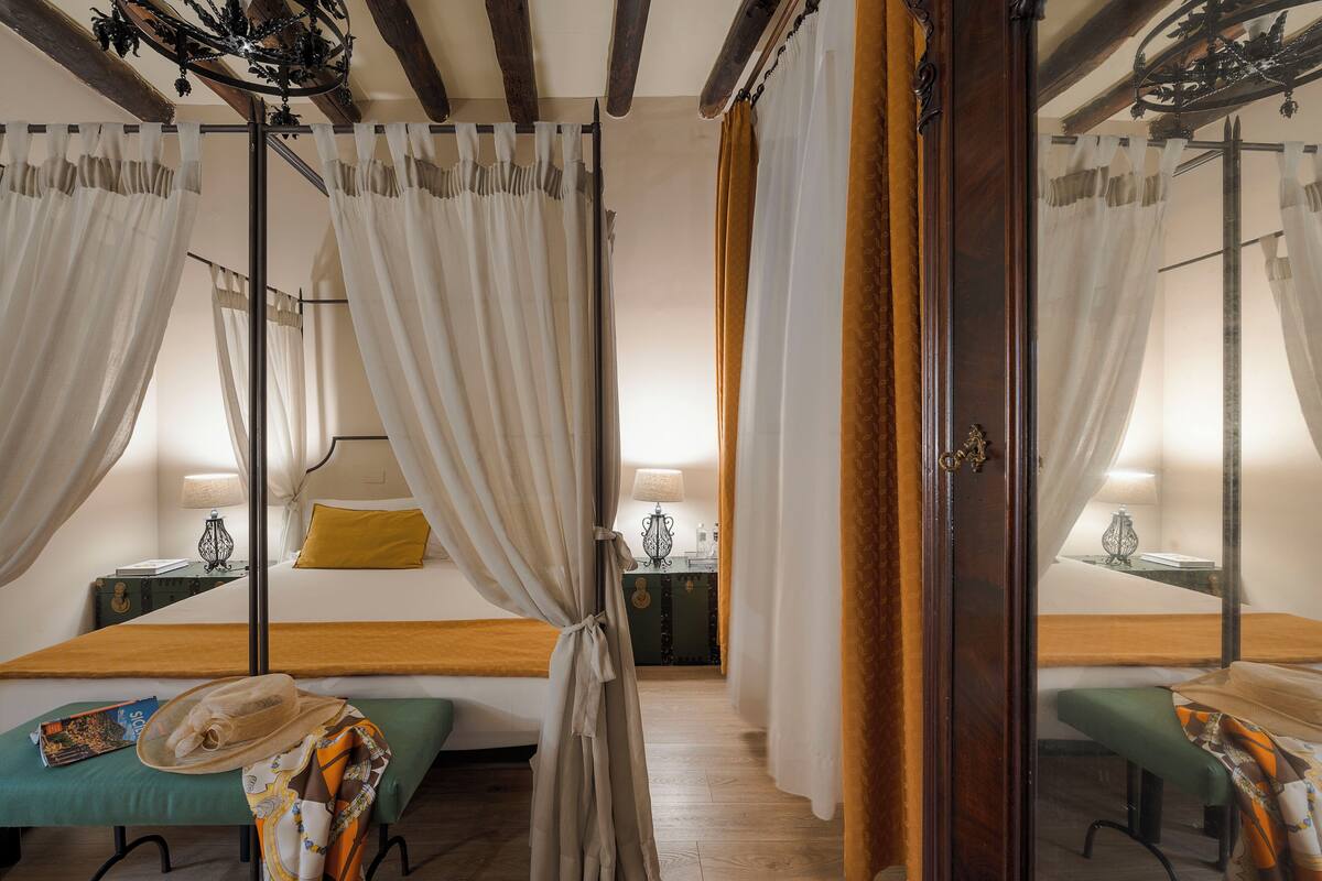 Quarto com cama de dossel, mesa de cabeceira com abajur e espelho.