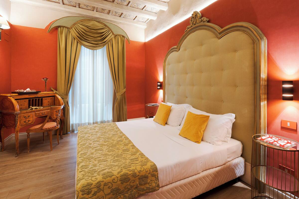 Quarto de hotel com uma cama grande, uma escrivaninha com cadeira e uma janela com cortinas.