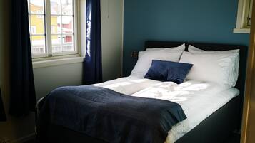 A bedroom with a bed, a window with curtains, a ceiling light, and a wall with a picture.