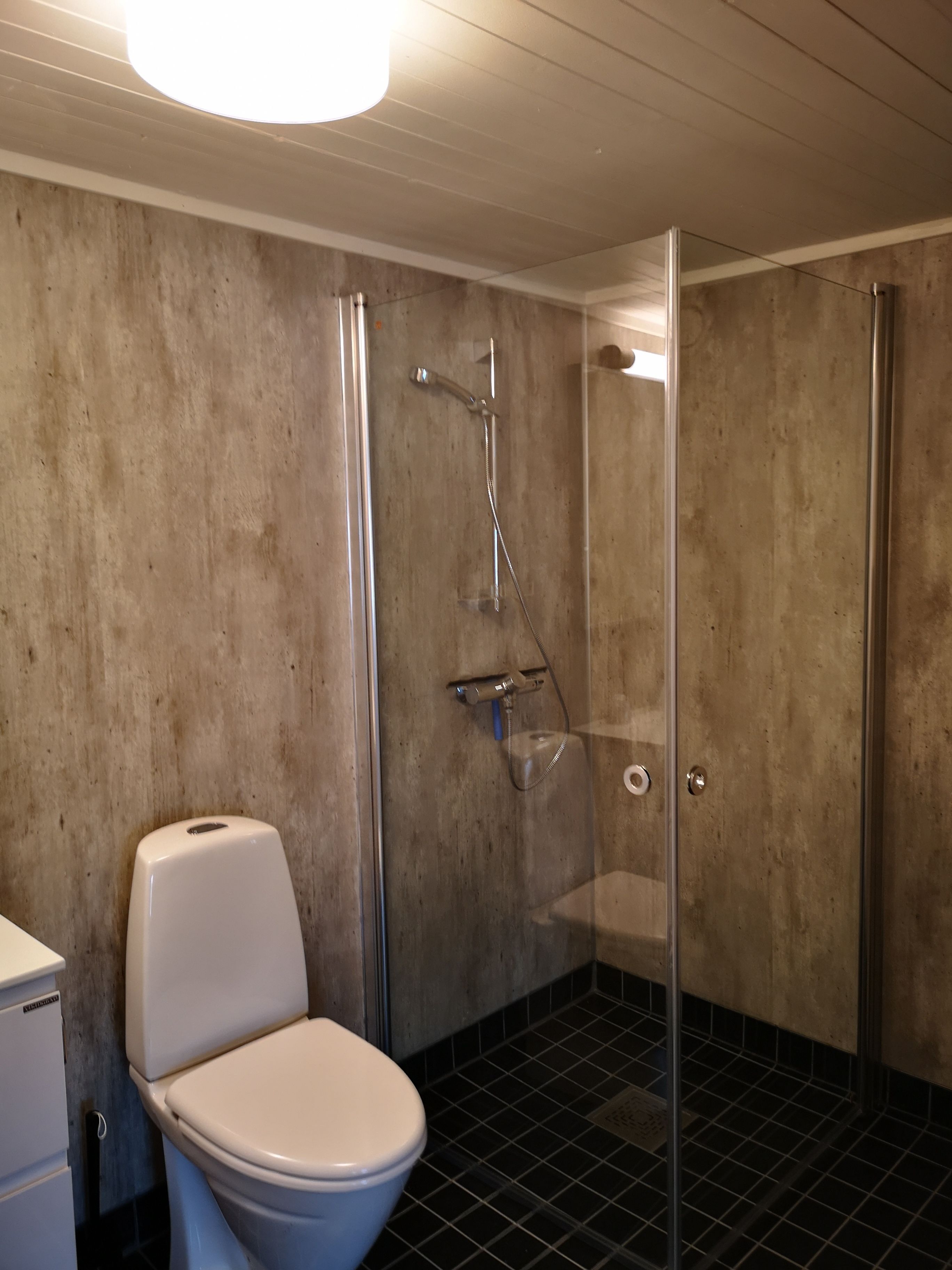 A bathroom with a toilet, a shower with a glass door, and a tiled floor.