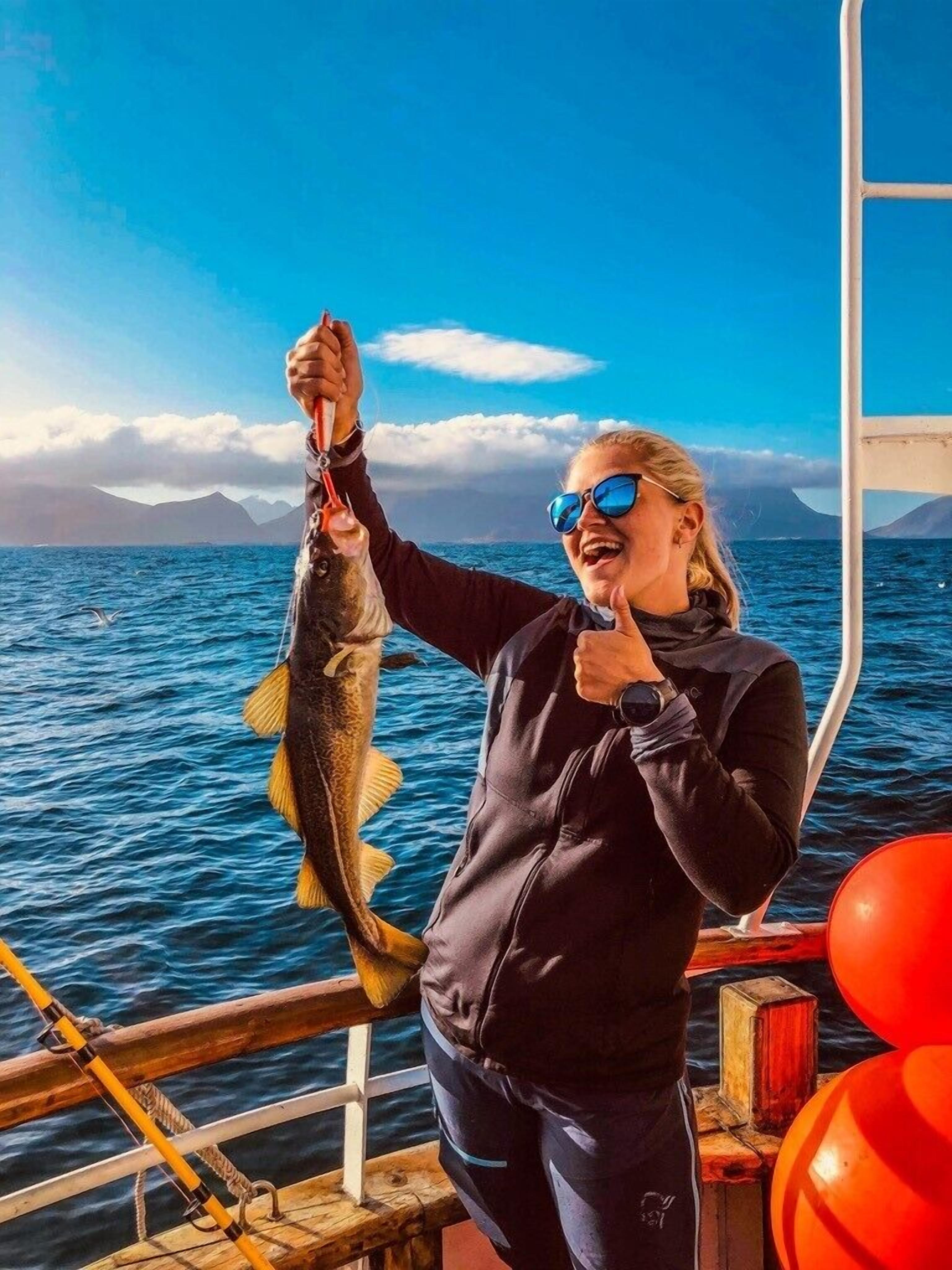Una persona sosteniendo un pez en un bote, con vista despejada al mar y montañas distantes.