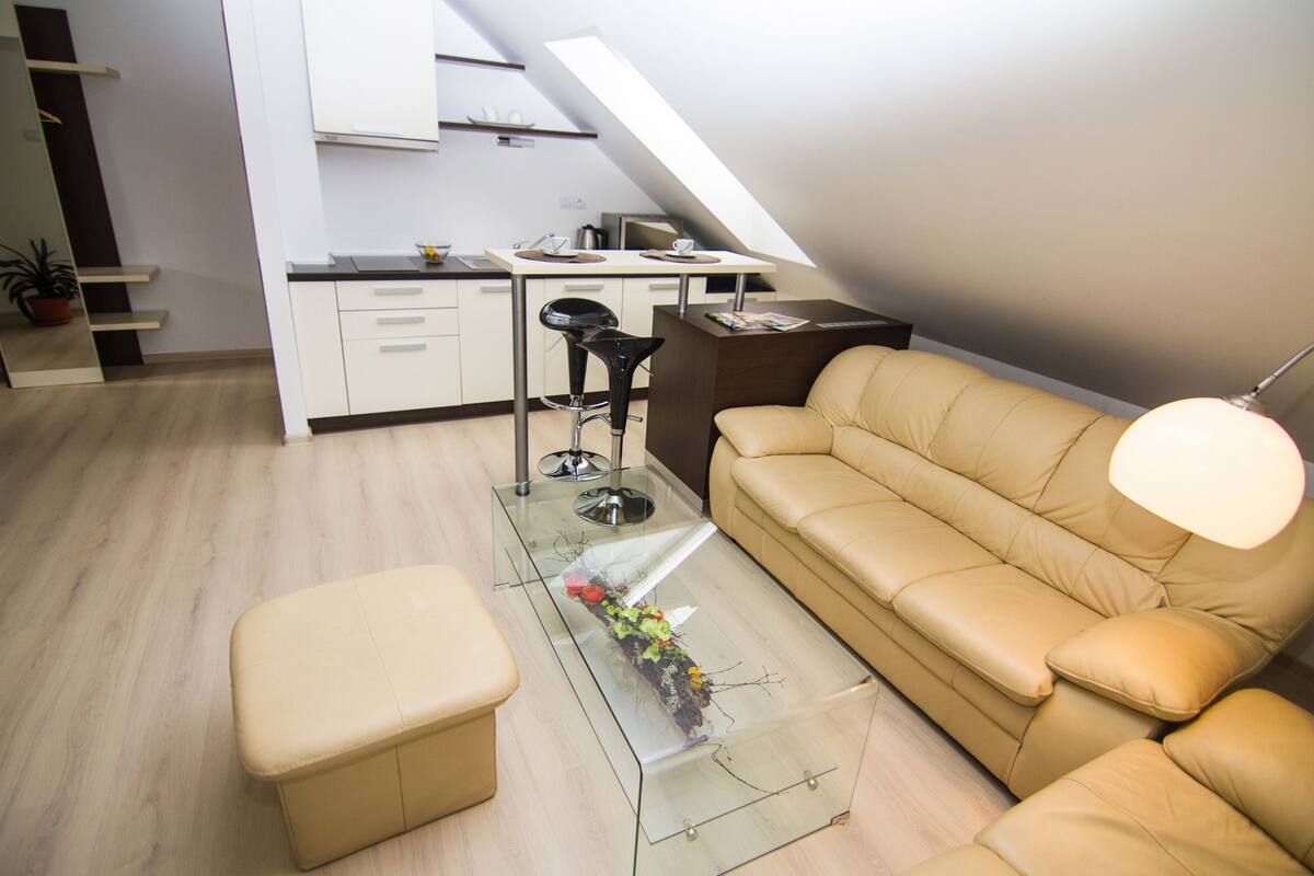 A modern living space with a glass coffee table, a beige sofa, and a kitchen area in the background.