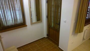 Un pasillo con suelo de baldosas, una puerta con cortina y una ventana con persianas.