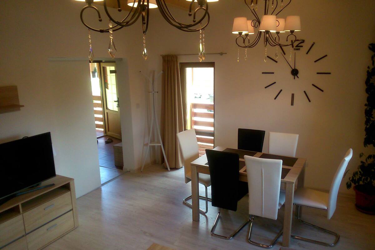 A dining area with a table, chairs, a TV, and a clock on the wall.