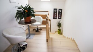 Una habitación moderna y bien iluminada, con una silla blanca, una mesita con una planta en maceta y una obra de arte en la pared.