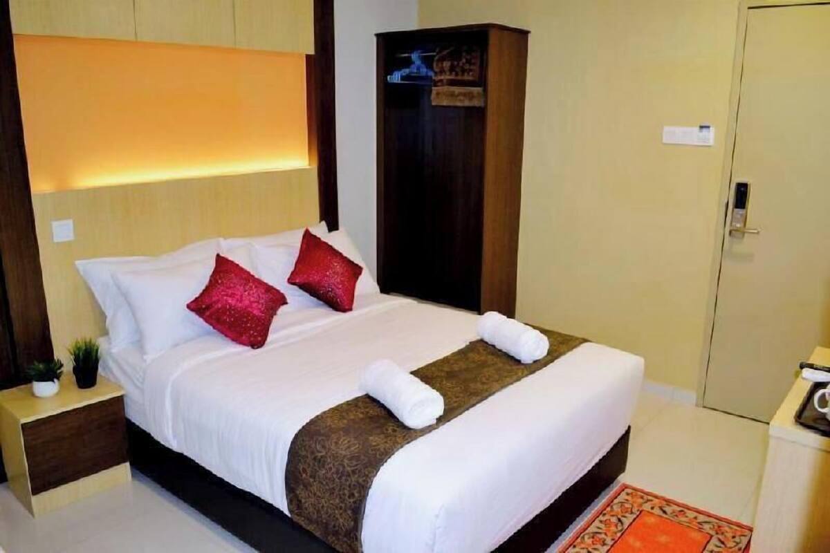 A neatly made bed with white linens and red pillows, a bedside table with a small plant, and a wardrobe with a hanging rod.