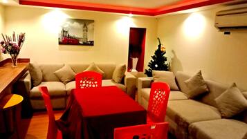 A living room with a sofa, a dining table with chairs, a Christmas tree, and a painting of a cityscape.