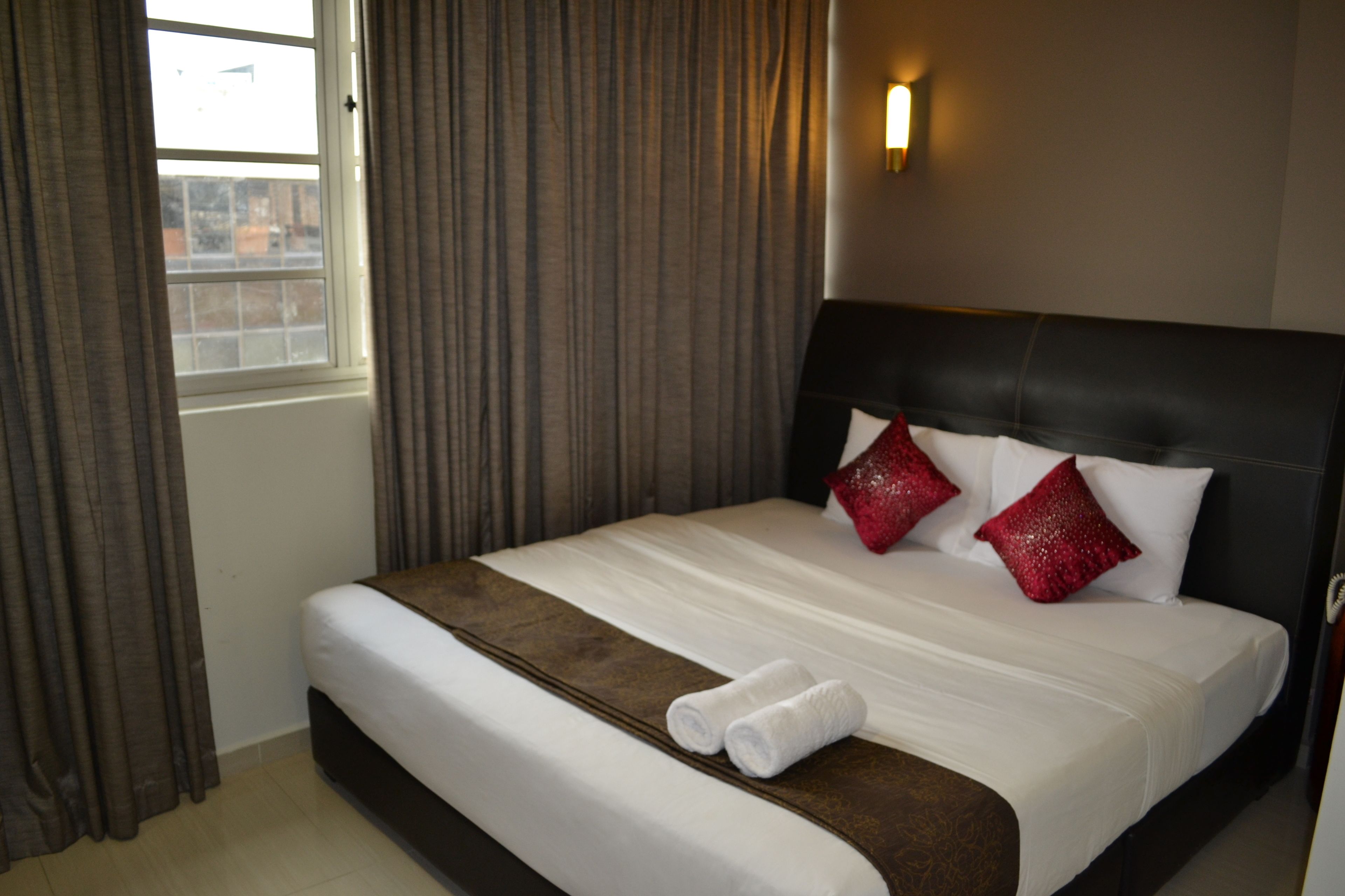 Une chambre d’hôtel avec un grand lit, une tête de lit et une fenêtre avec des rideaux.