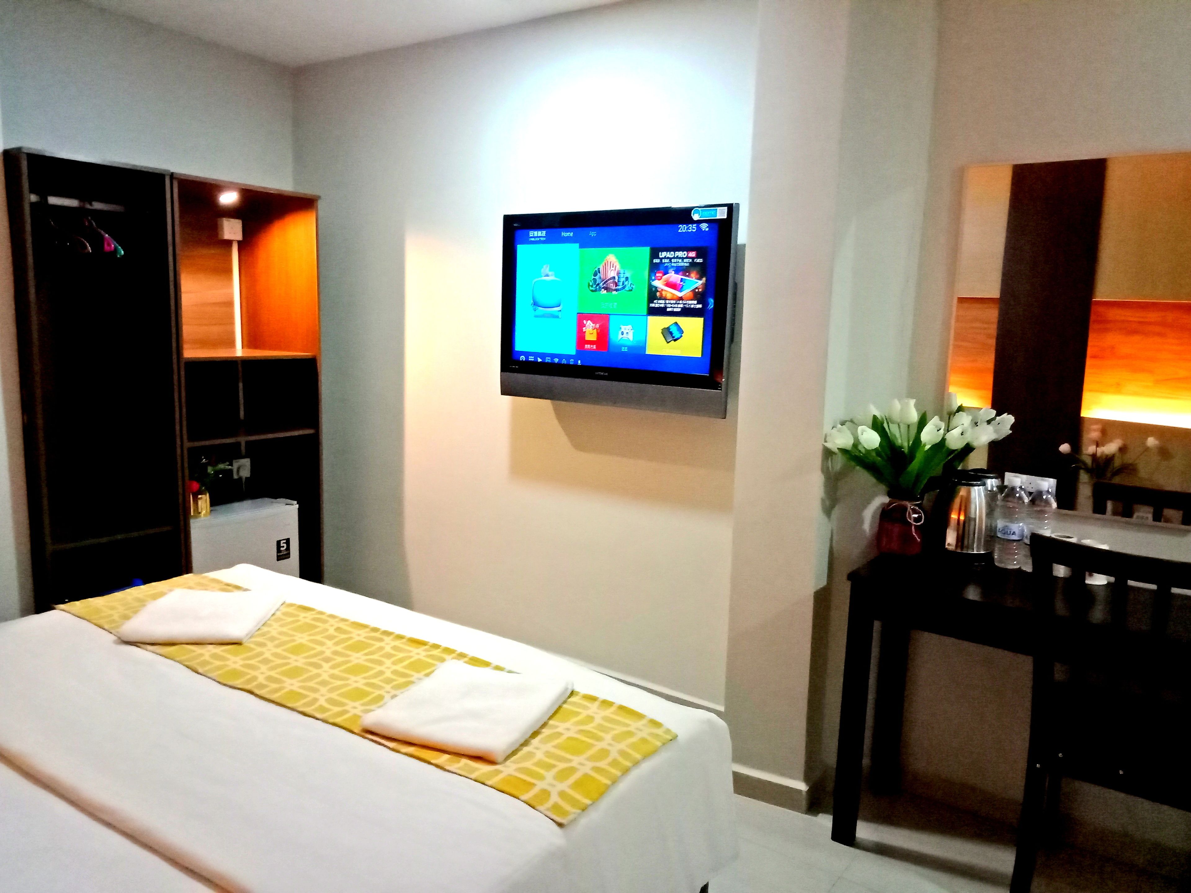 Habitación de hotel con cama, televisor montado en la pared, escritorio con un florero y armario.