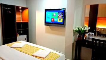 Habitación de hotel con cama, televisor montado en la pared, escritorio con un florero y armario.