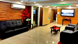 Un espace d’accueil moderne avec un canapé en cuir noir, une plante décorative rouge, un téléviseur à écran plat et un mur en bois.