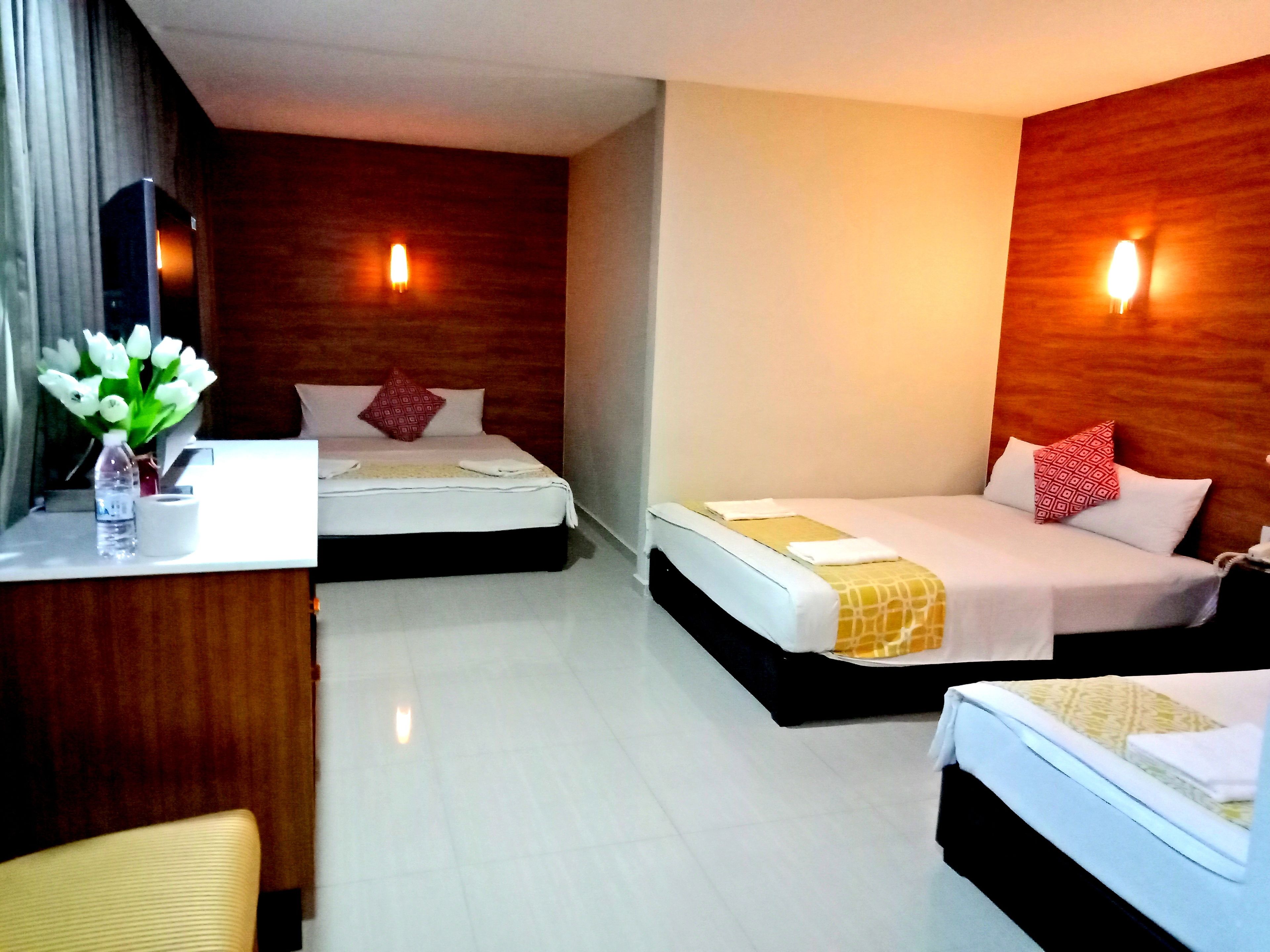 Una habitación de hotel con dos camas, un escritorio y un florero con flores.