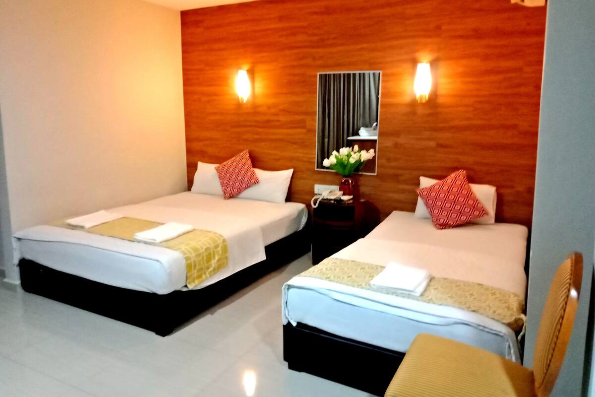 A hotel room with two beds, a wooden headboard, a nightstand with a vase of flowers, and a mirror.