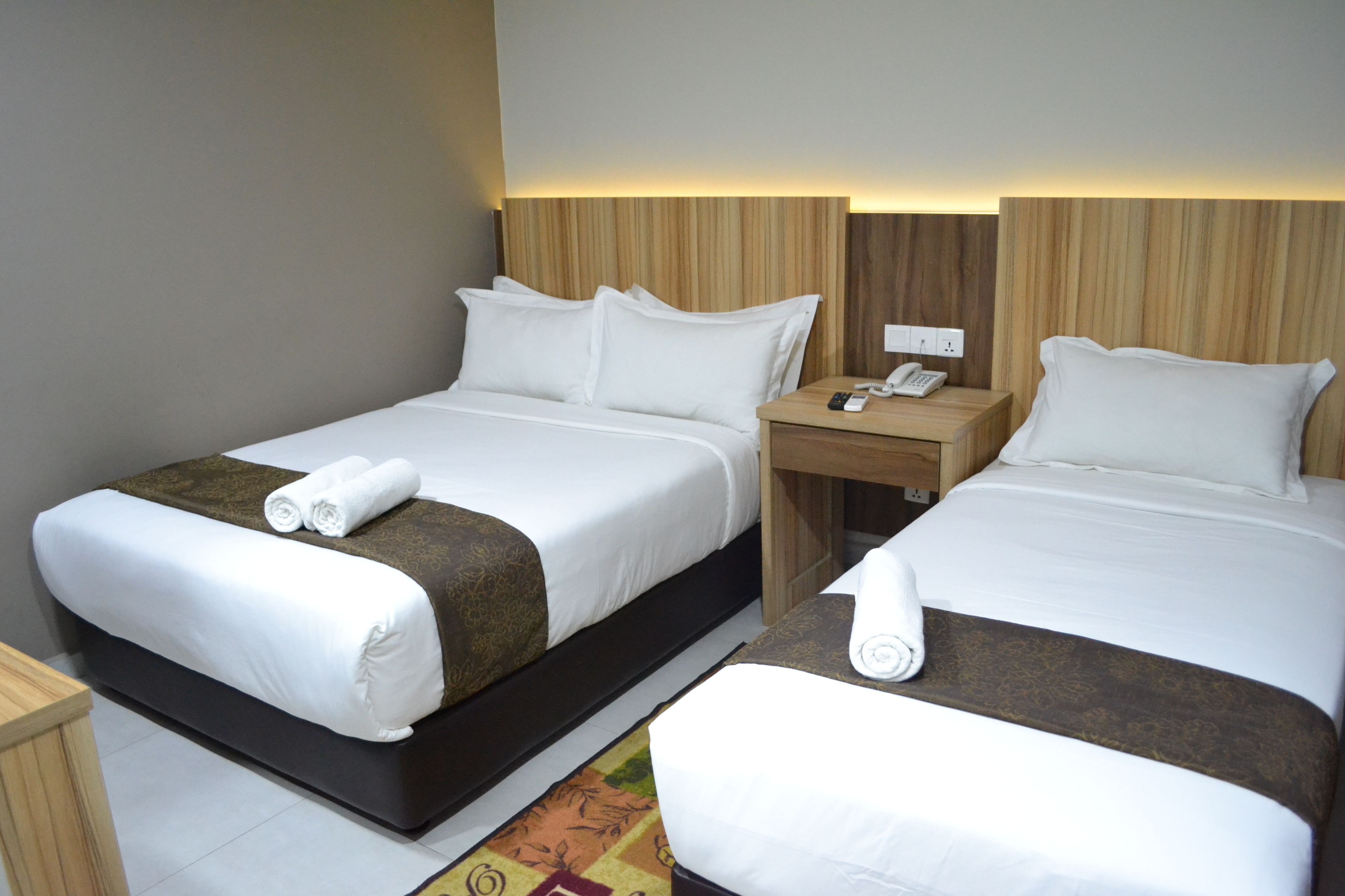 A hotel room with two beds, a nightstand with a phone, and a wall-mounted light.