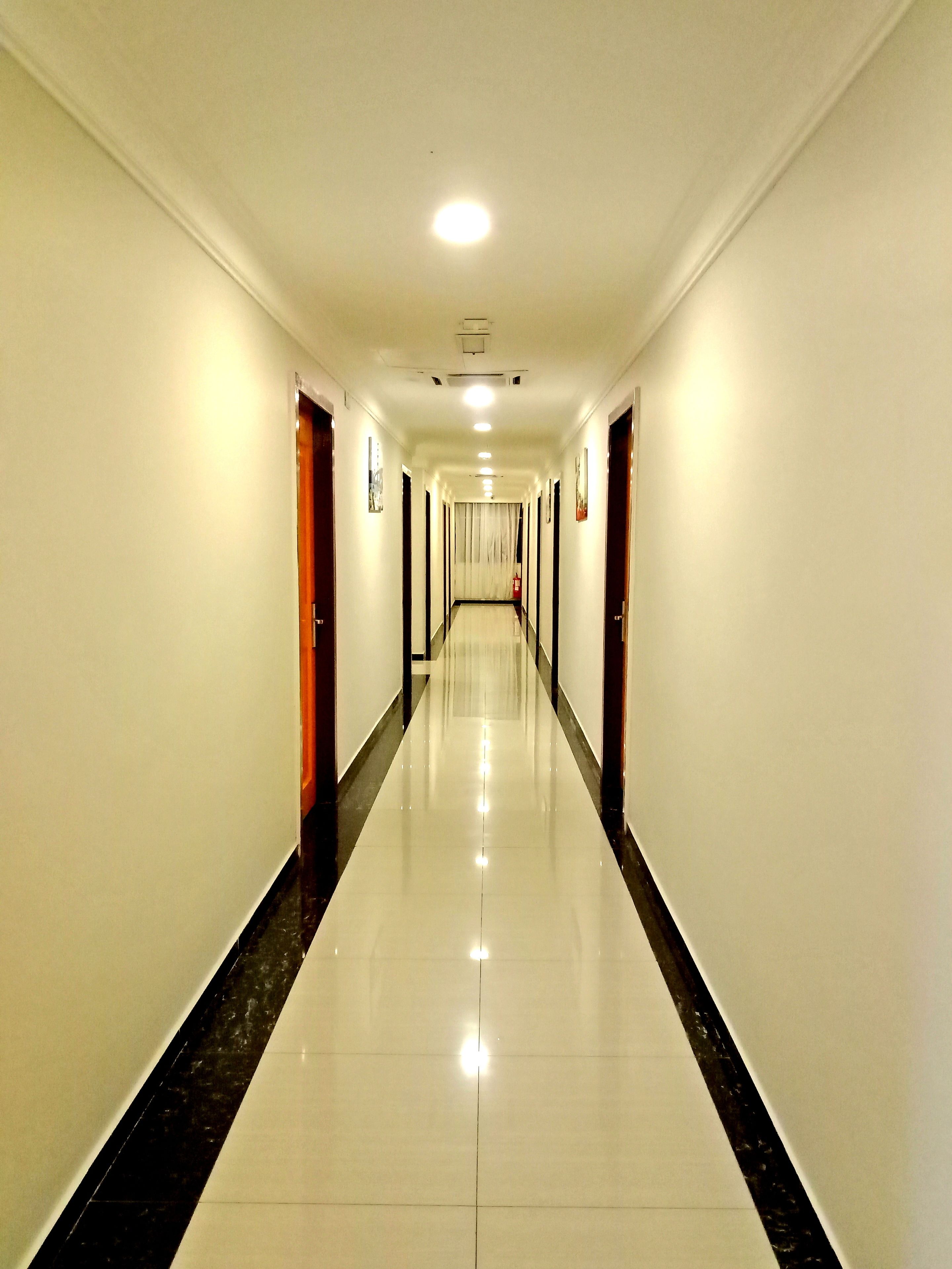 Un pasillo largo y bien iluminado, con paredes blancas y piso brillante, que conduce a una puerta al final.