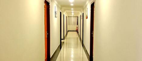 Un pasillo largo y bien iluminado, con paredes blancas y piso brillante, que conduce a una puerta al final.