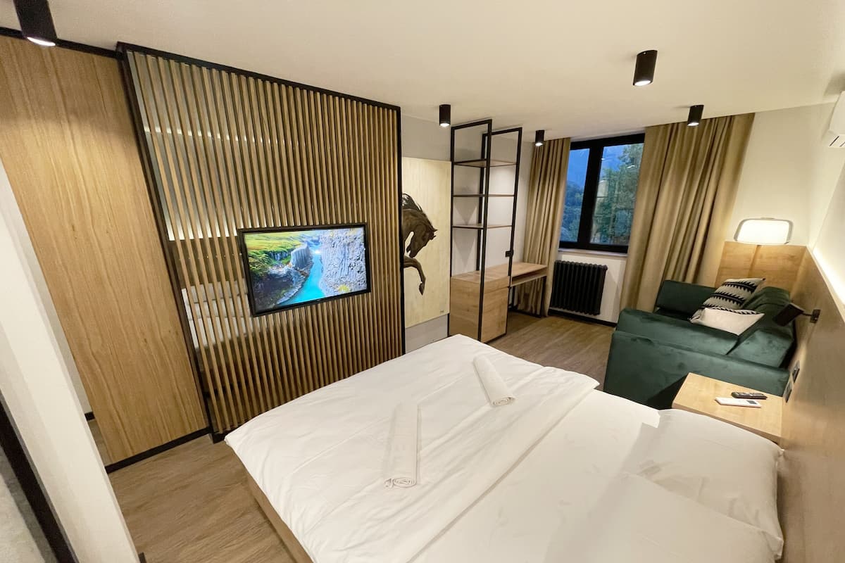 Hotelkamer met een bed, een televisie bevestigd aan een houten paneel, een groene bank en een raam met gordijnen.