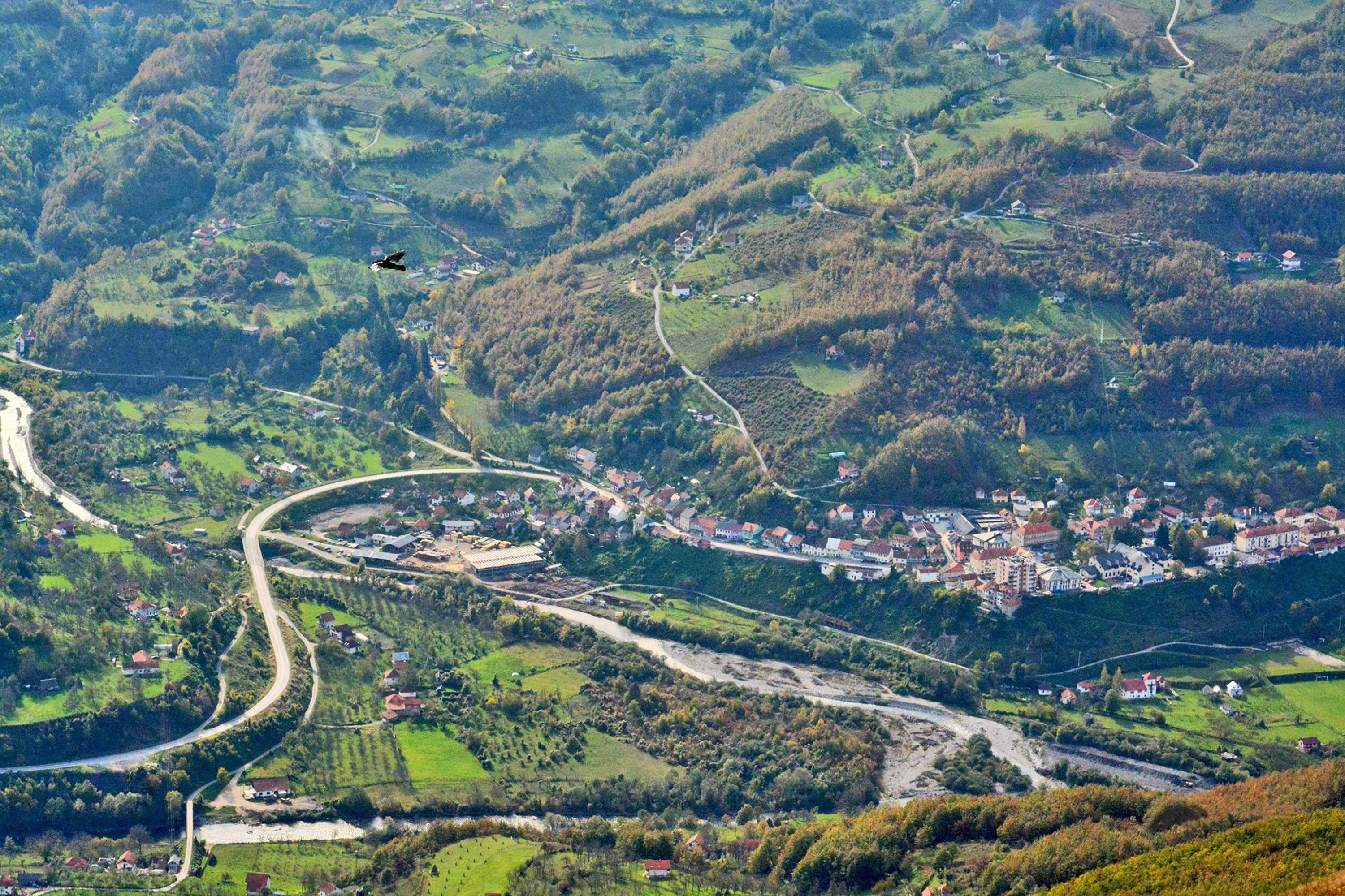 Paisaje rural con carreteras sinuosas, casas dispersas y un helicóptero volando.