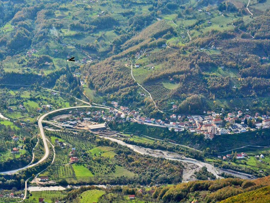 Paisaje rural con carreteras sinuosas, casas dispersas y un helicóptero volando.
