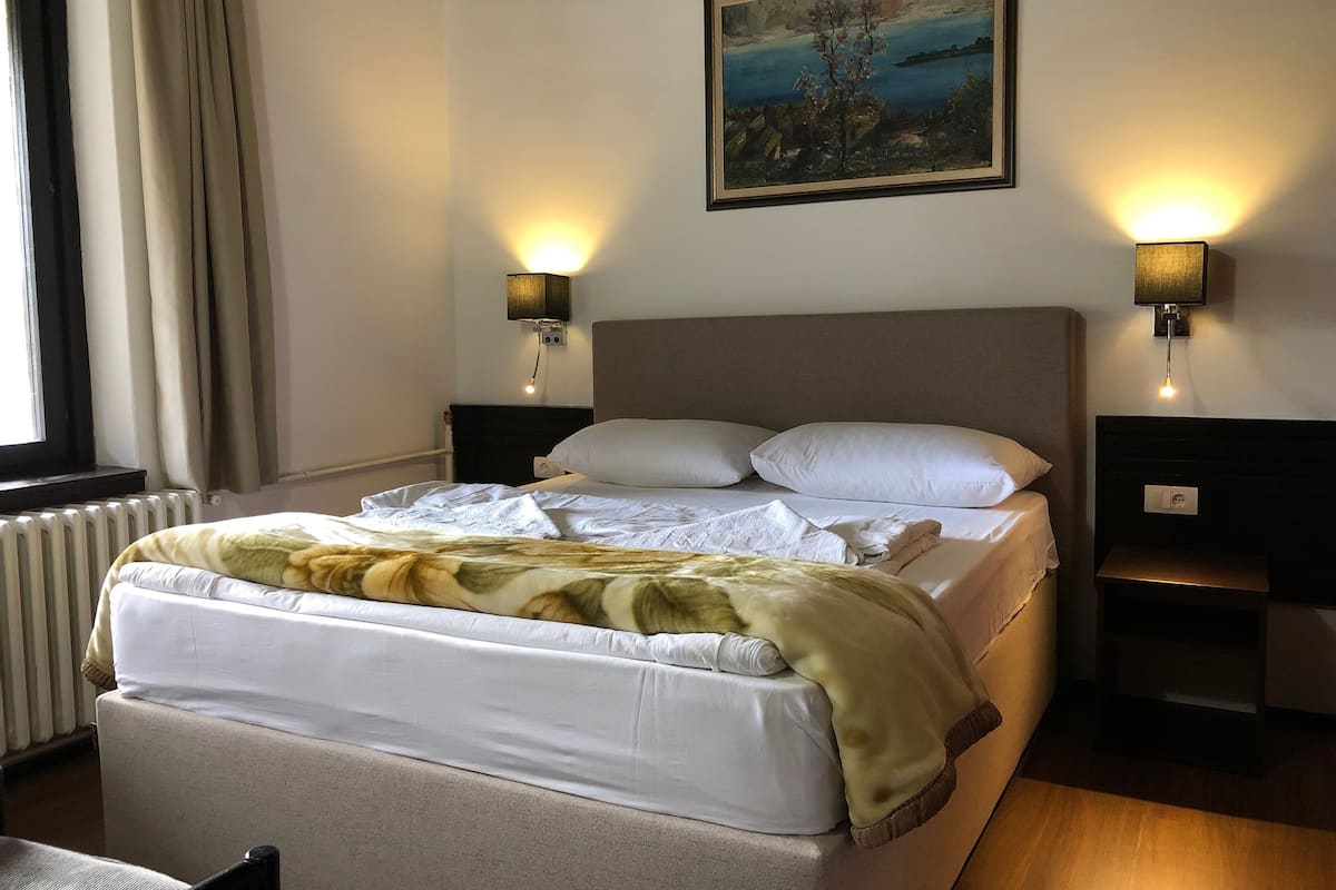 Een hotelkamer met een bed, twee nachtkastjes, een schilderij aan de muur en een raam met gordijnen.