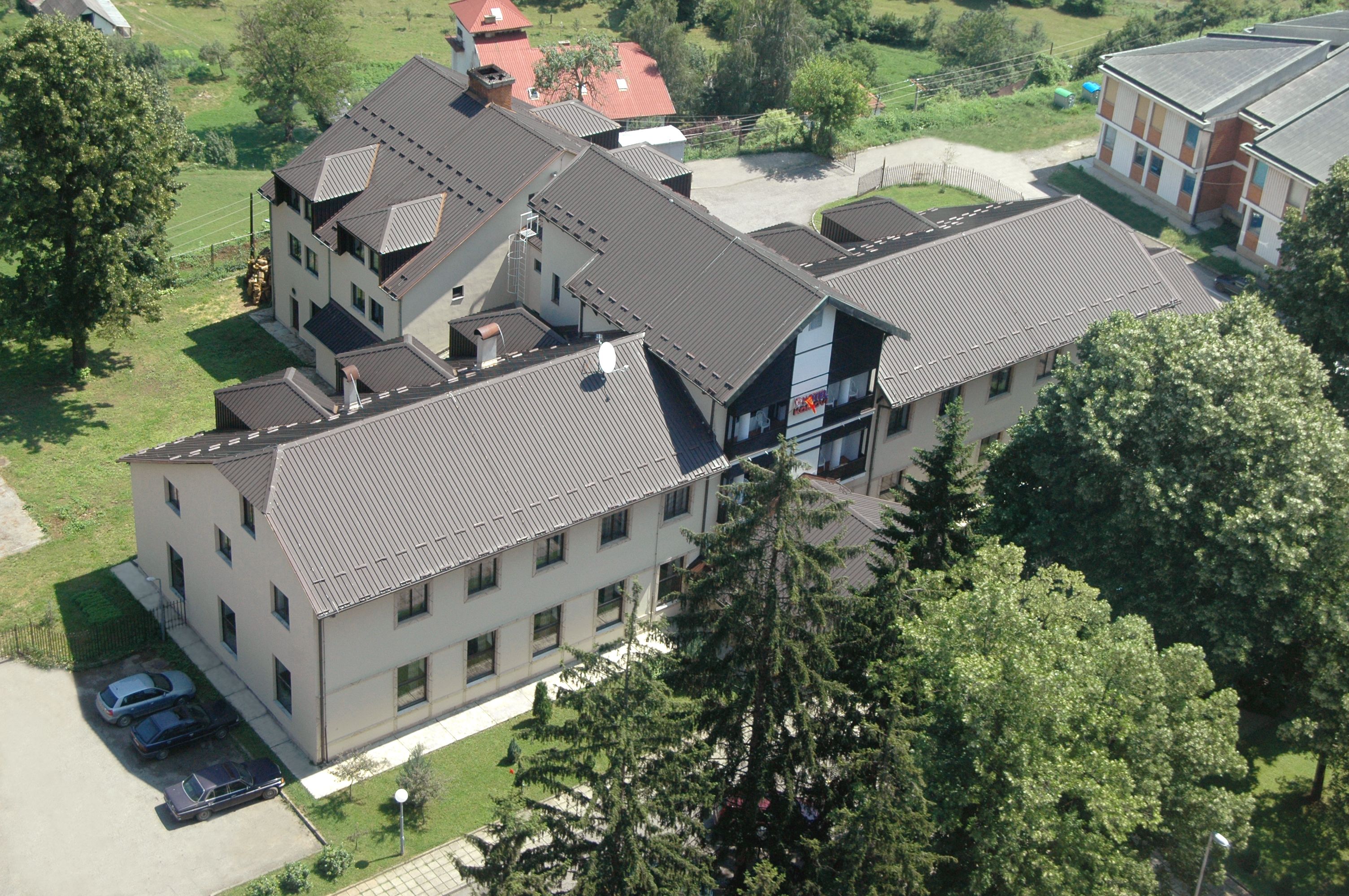 An aerial view of a multi-story building with a flat roof, surrounded by greenery and trees.