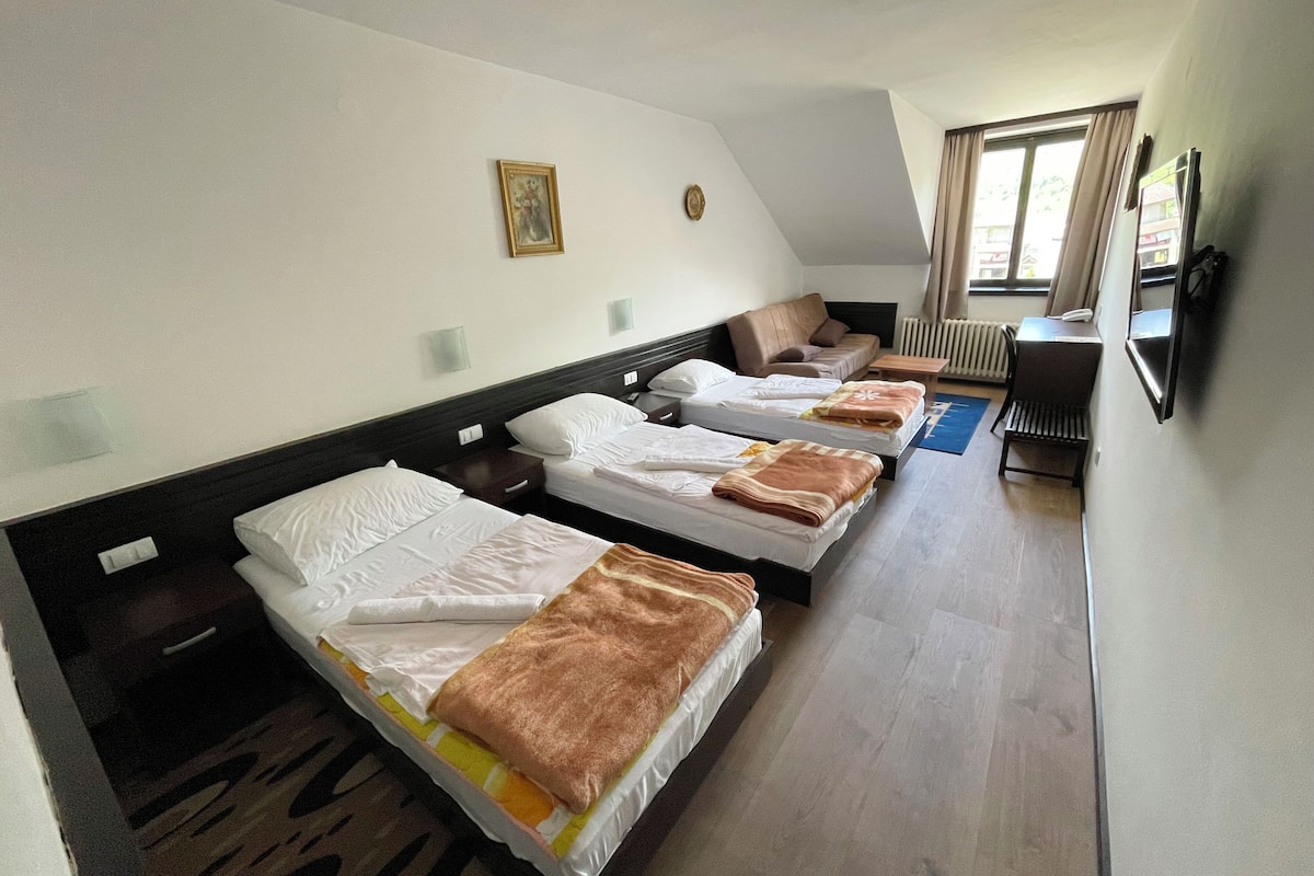 Een hotelkamer met drie eenpersoonsbedden, een bank, een bureau en een televisie.