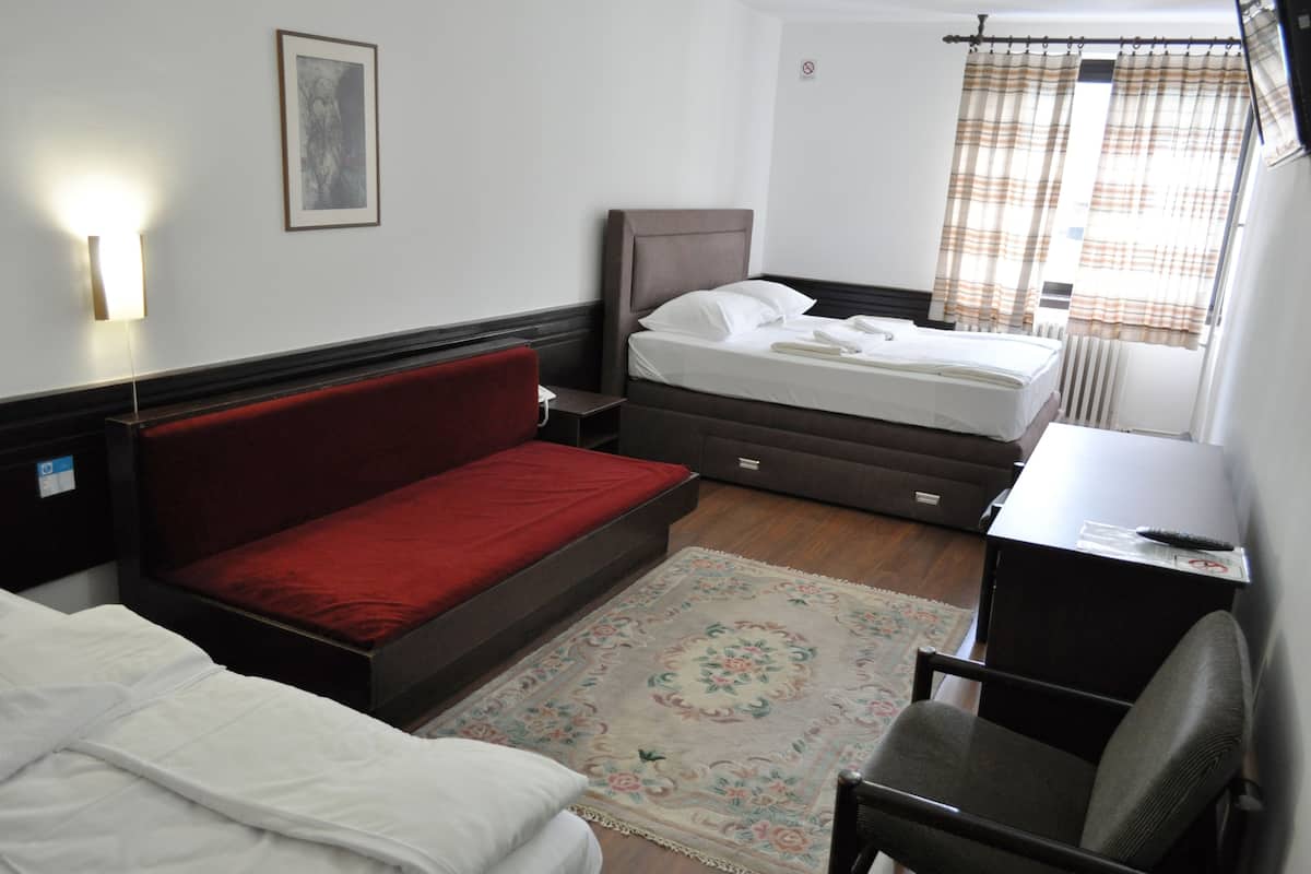Een hotelkamer met een bed, een bureau, een stoel, een rode bank, een vloerkleed en een wandlamp.