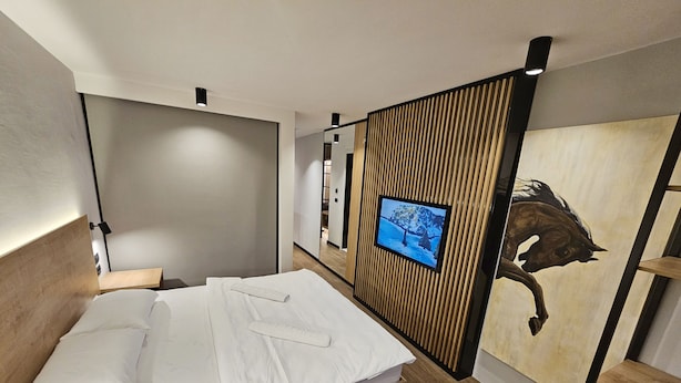 Una habitación de hotel moderna con una cama, un televisor montado en un panel de madera y un cuadro grande de un caballo.