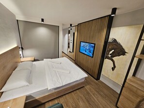 Een moderne hotelkamer met een bed, een aan een houten paneel bevestigde televisie en een groot schilderij van een paard.