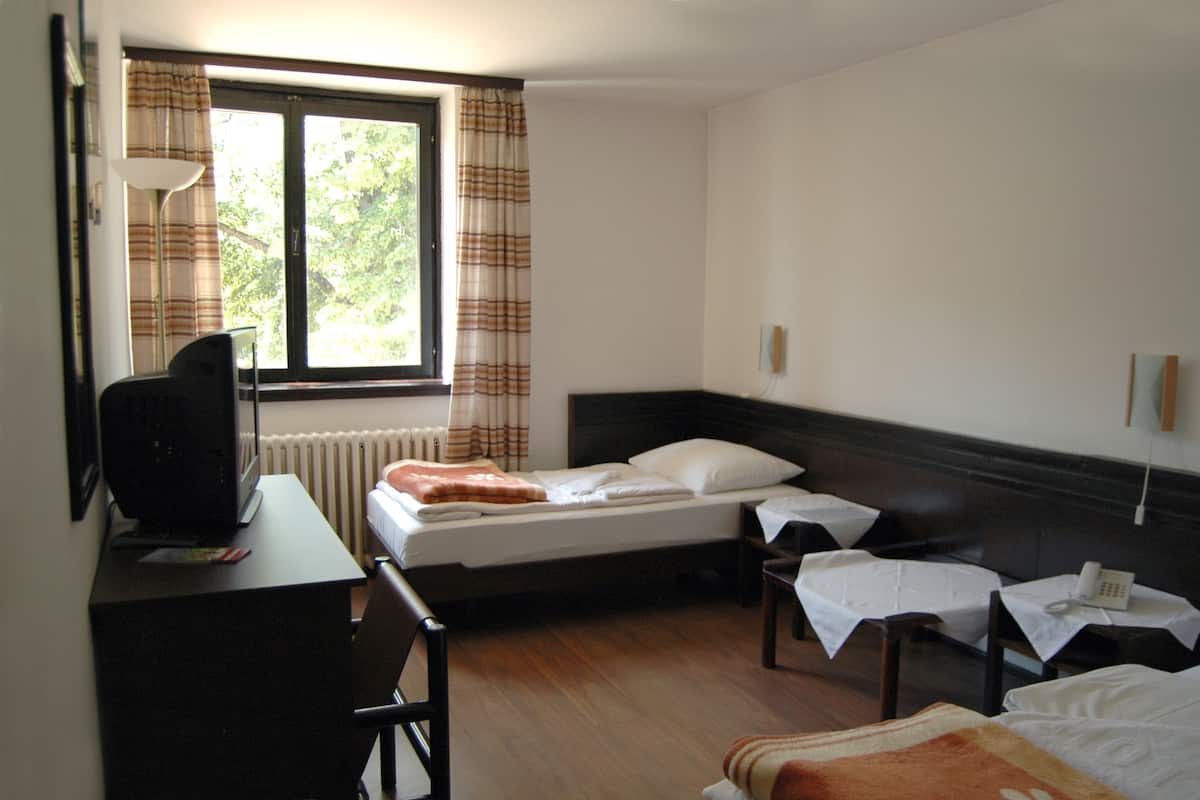 Een hotelkamer met een bed, een bureau met een computer, een stoel, een klein tafeltje met een telefoon en een raam met gordijnen.