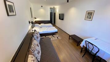 A modern hotel room with a sofa bed, a small table with a chair, and a TV mounted on the wall.