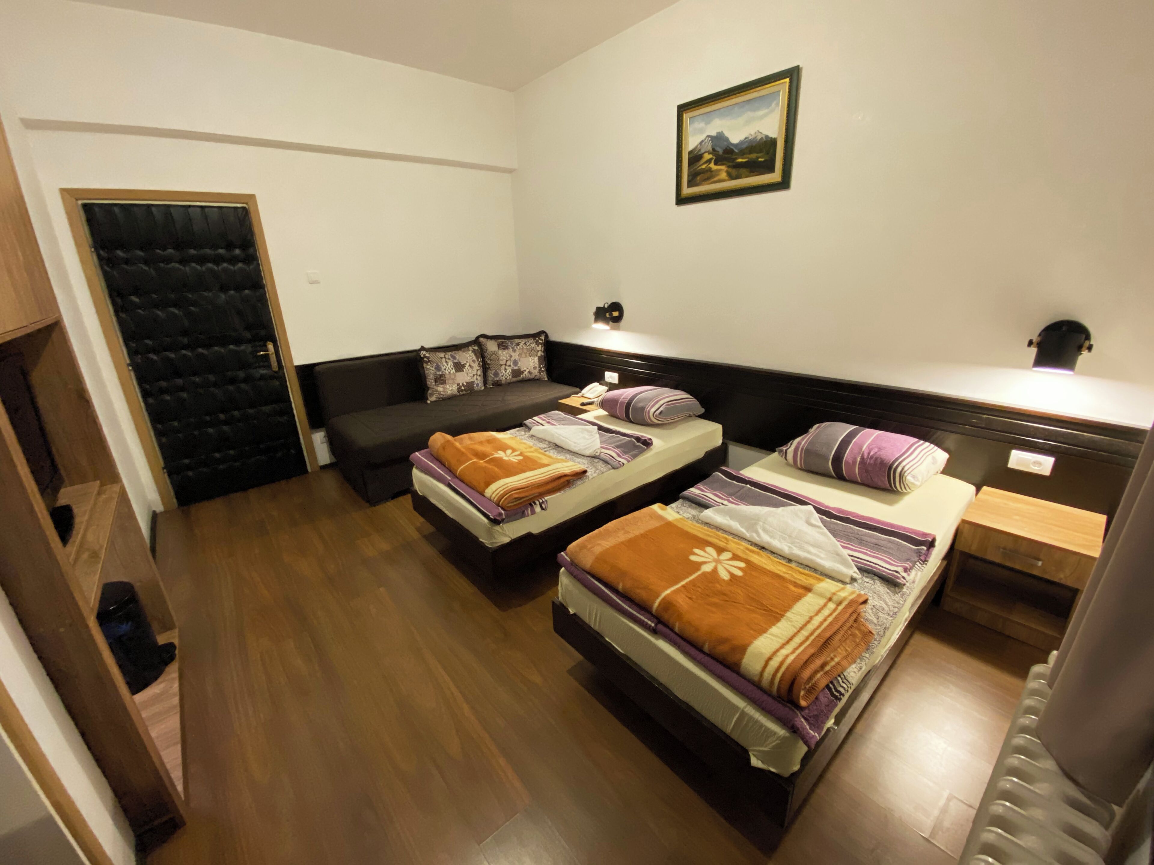 A room with two beds, a sofa, a door, and a painting on the wall.