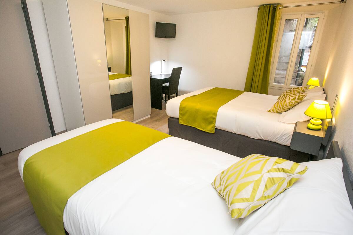 Une chambre d’hôtel avec deux lits, un bureau et une télévision.
