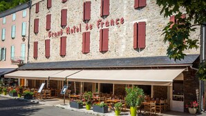 Un bâtiment en pierre sur lequel on peut lire l’inscription « Grand Hôtel de France », et une terrasse avec des tables et des chaises.