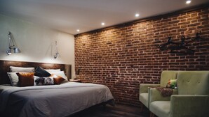 A modern bedroom with a brick wall, a bed with multiple pillows, a green armchair, and a small rug. - Les Aires en Scènes (Epagne-Epagnette)