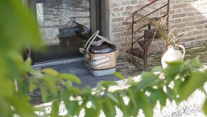 A rustic building entrance with a metal door, a wooden chair, and a potted plant. - Les Aires en Scènes (Epagne-Epagnette)