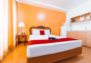 A hotel room with a bed, a desk, a lamp, and a kitchenette.