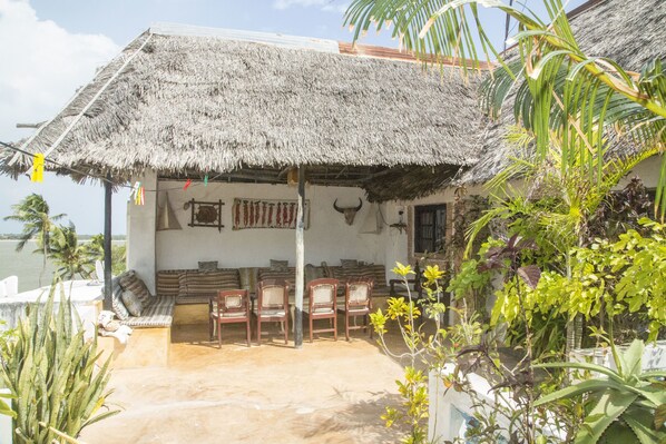 A thatched-roof outdoor seating area with chairs and cushions, overlooking a body of water.