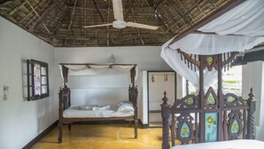 A room with a wooden four-poster bed, a ceiling fan, and a thatched roof. - Pwani Guest House (Lamu)