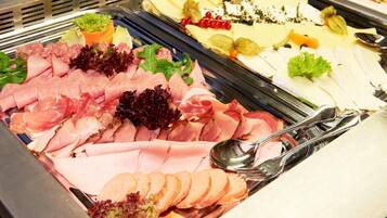 A buffet with various meats and cheeses, including ham, salami, and different types of cheese, arranged on a metal tray.