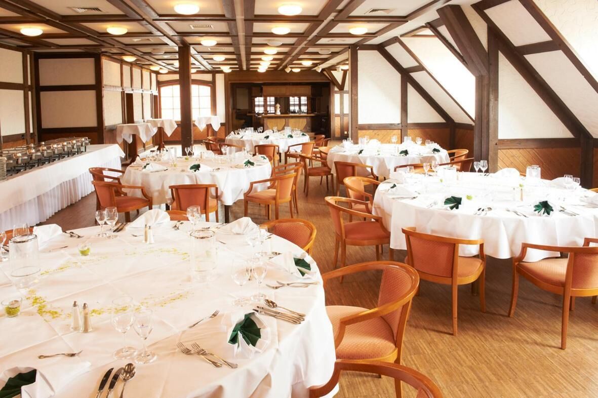 A banquet hall with round tables set for dining, wooden chairs, and a long buffet table.